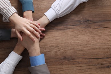 Photo of Business concept. Group of people stacking hands at wooden table, top view. Space for text