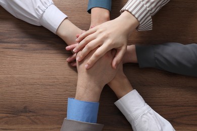 Photo of Business concept. Group of people stacking hands at wooden table, top view