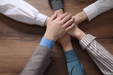 Photo of Business concept. Group of people stacking hands at wooden table, top view