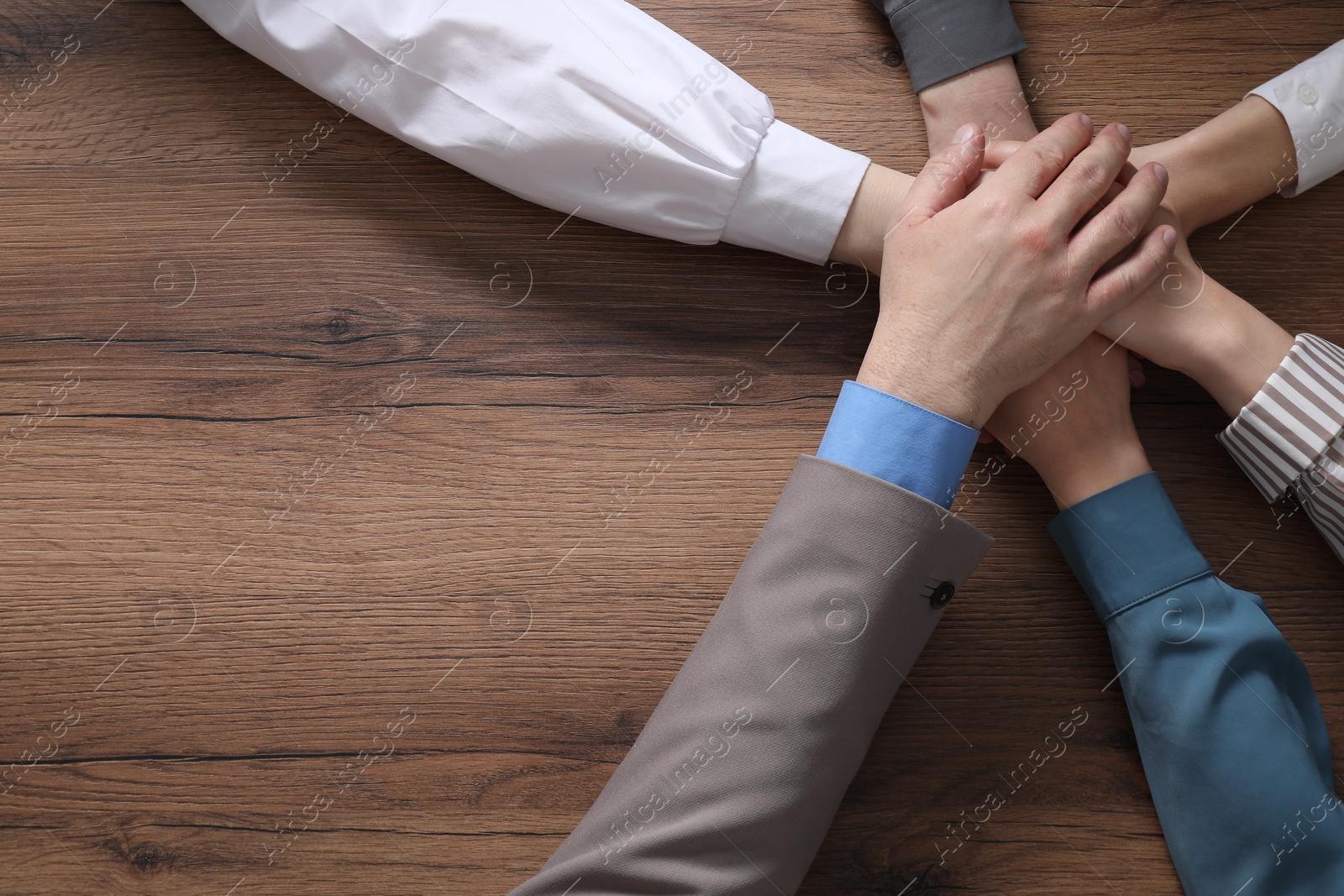 Photo of Business concept. Group of people stacking hands at wooden table, top view. Space for text