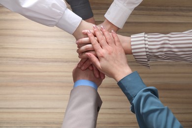 Photo of Business concept. Group of people stacking hands at wooden table, top view