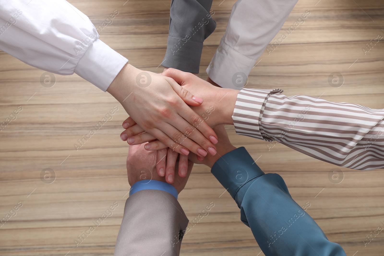 Photo of Business concept. Group of people stacking hands at wooden table, top view