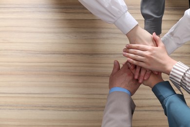 Photo of Business concept. Group of people stacking hands at wooden table, top view. Space for text