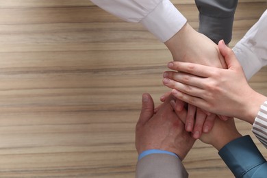 Photo of Business concept. Group of people stacking hands at wooden table, top view. Space for text