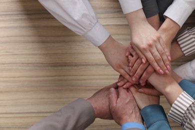 Photo of Business concept. Group of people stacking hands at wooden table, top view. Space for text