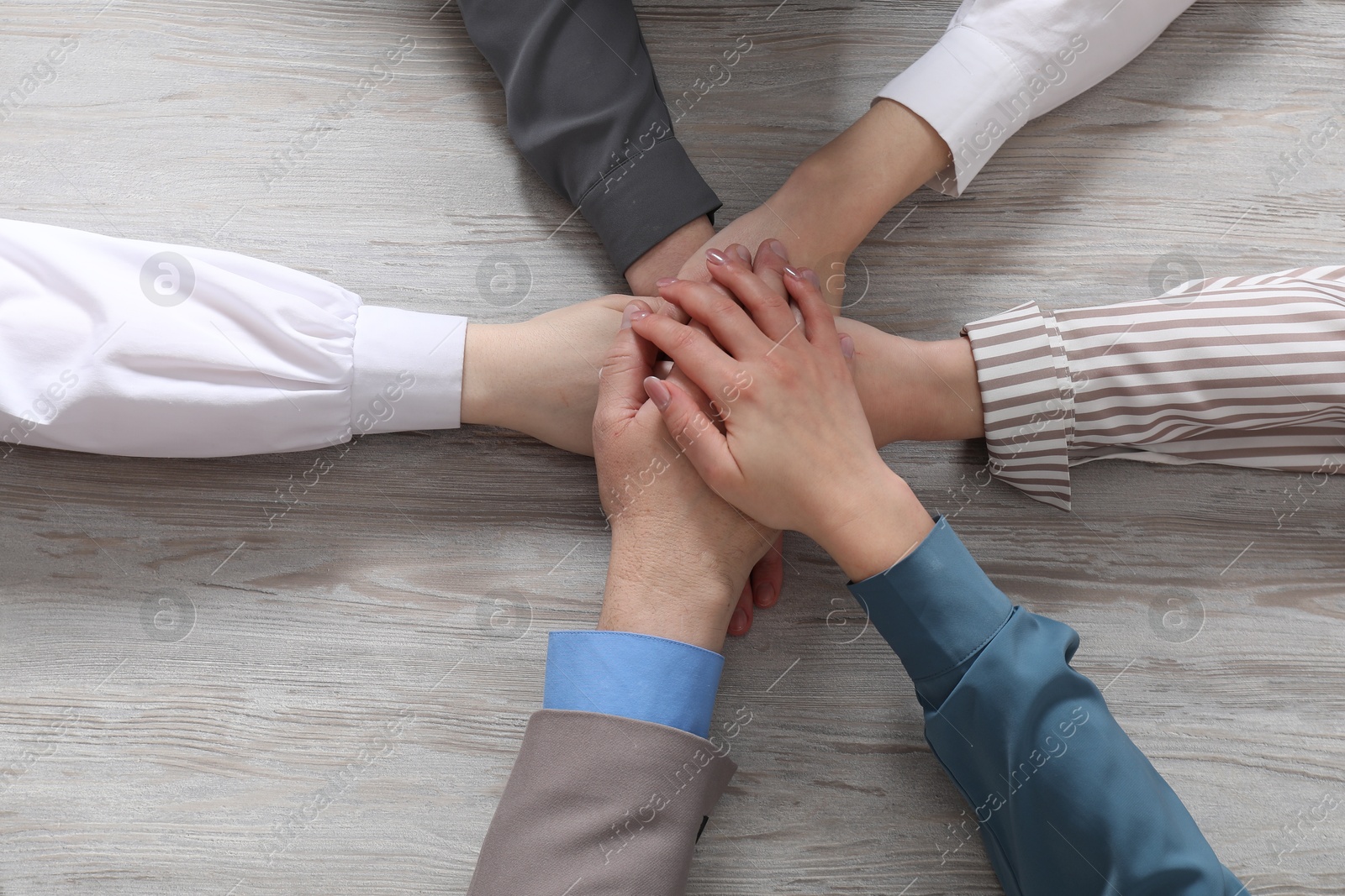 Photo of Business concept. Group of people stacking hands at light grey wooden table, top view