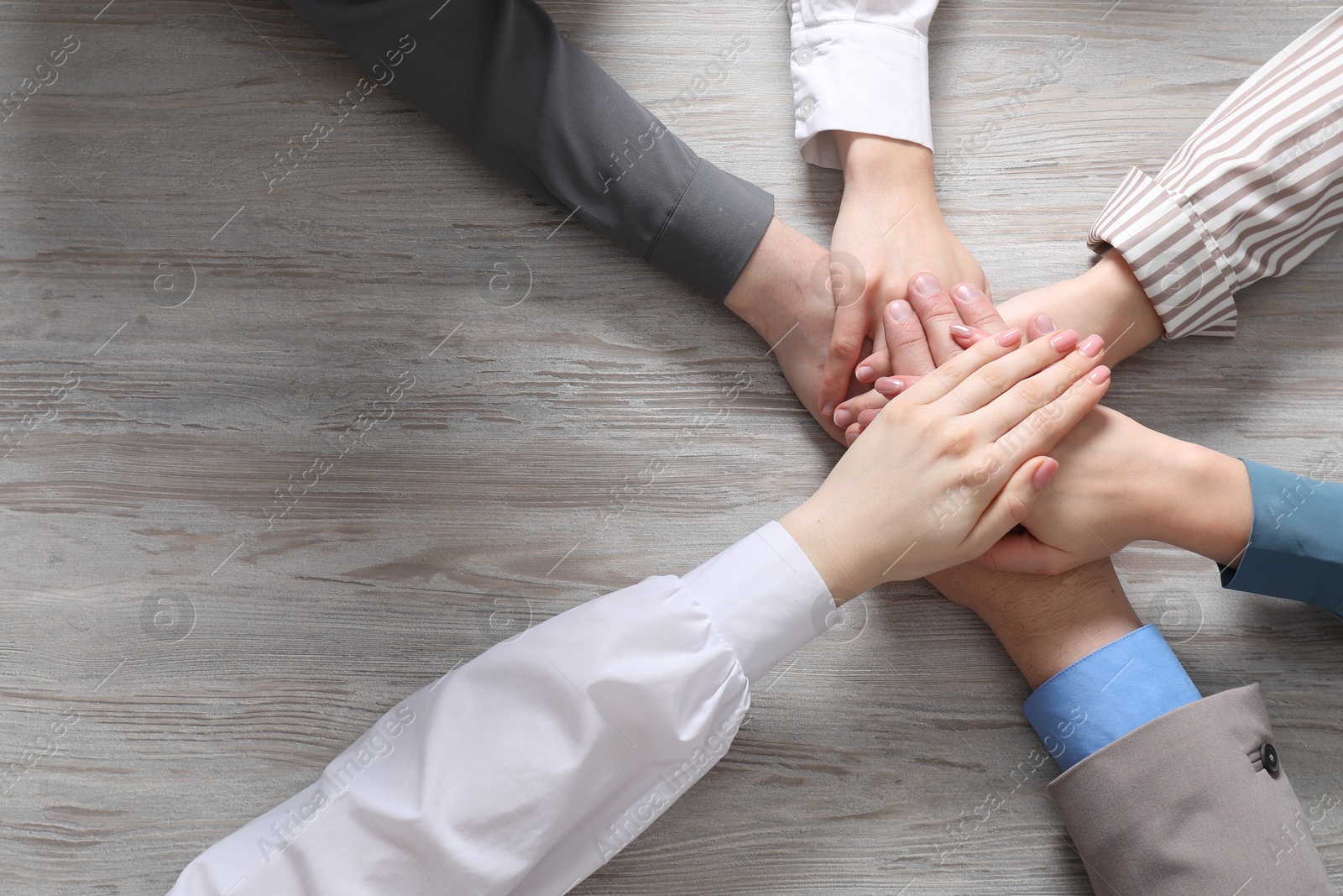 Photo of Business concept. Group of people stacking hands at light grey wooden table, top view