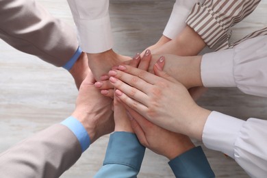 Photo of Business concept. Group of people stacking hands at light wooden table, top view