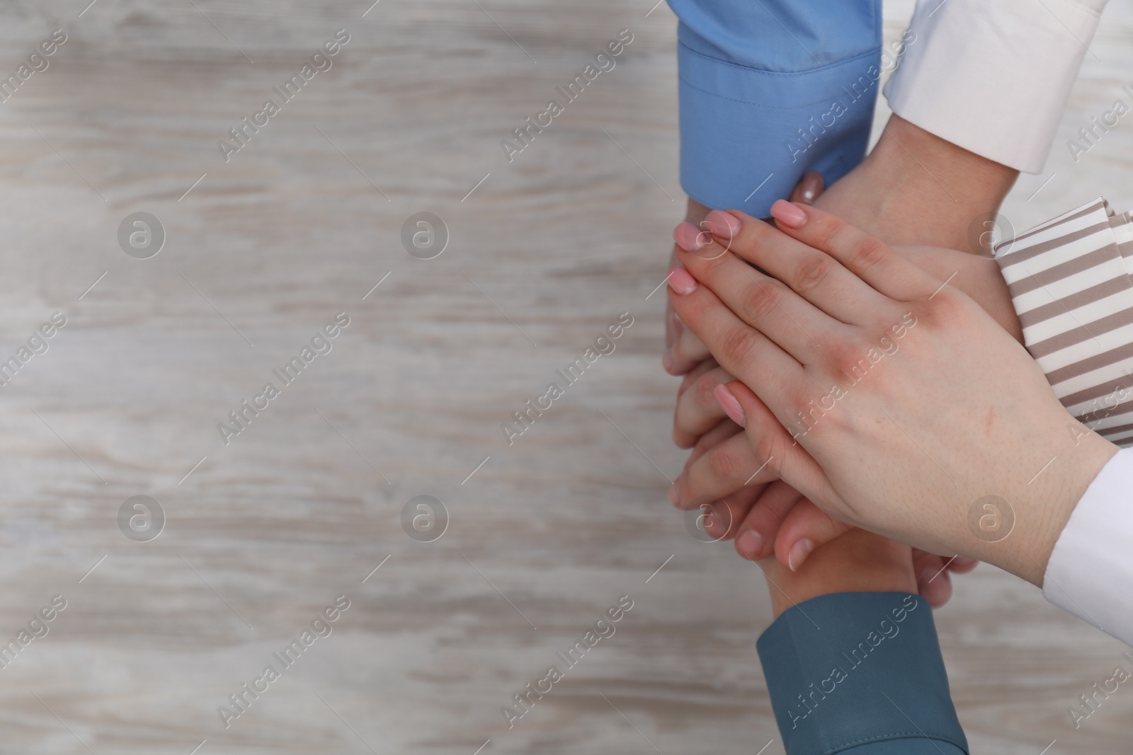 Photo of Business concept. Group of people stacking hands at light wooden table, top view. Space for text