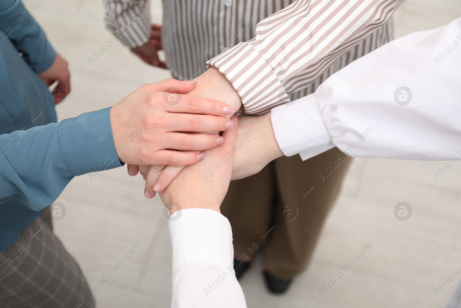 Photo of Business concept. Group of people stacking hands indoors, above view