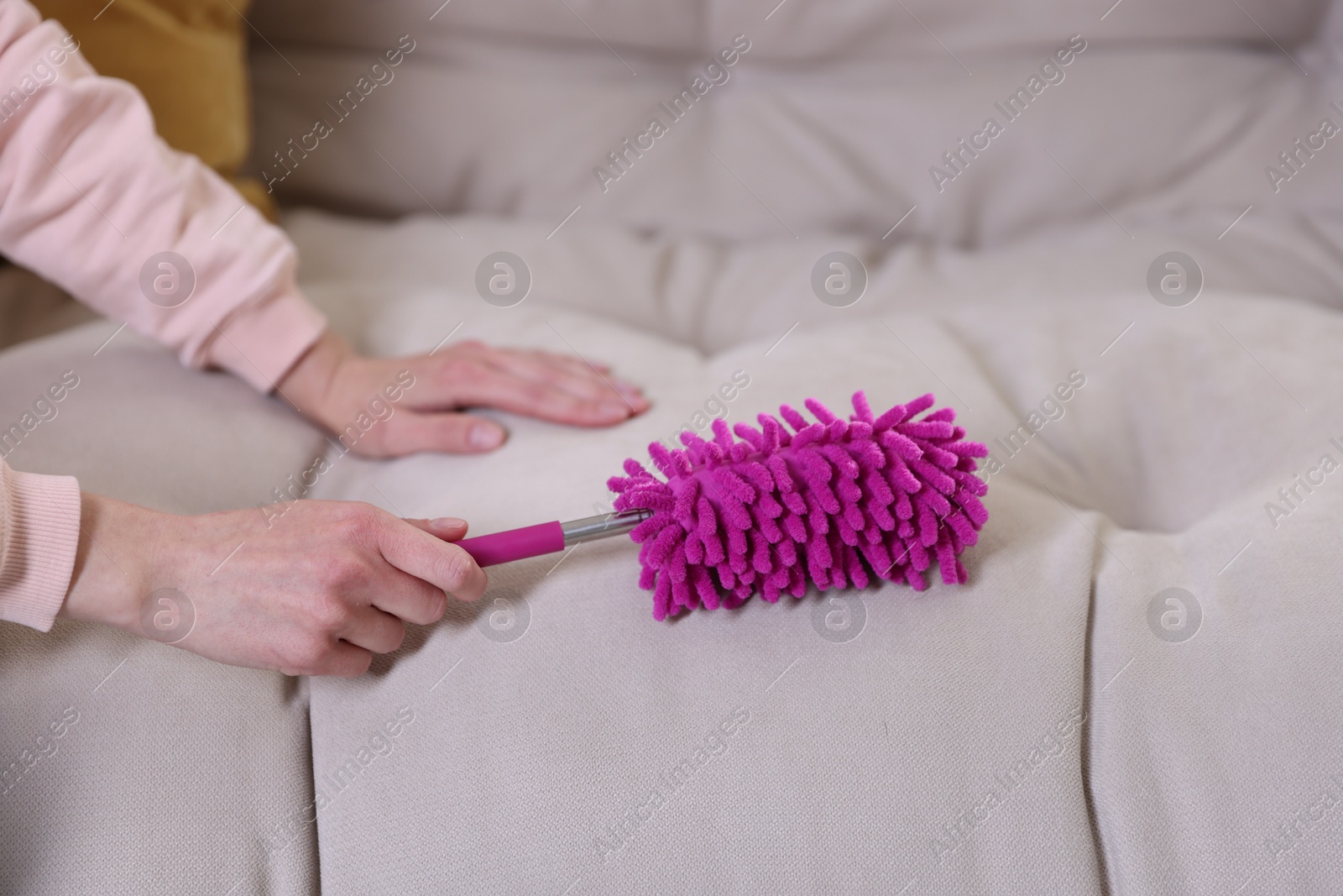 Photo of Woman cleaning sofa with duster at home, closeup