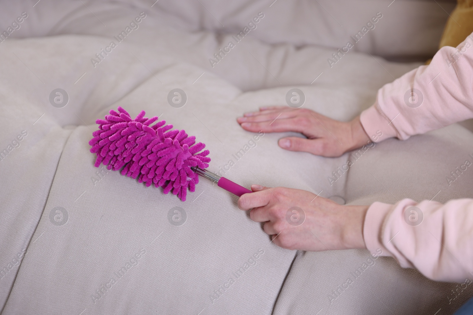 Photo of Woman cleaning sofa with duster at home, closeup