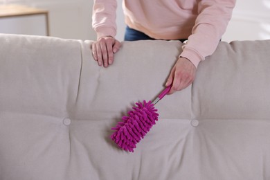 Photo of Woman cleaning sofa with duster at home, closeup