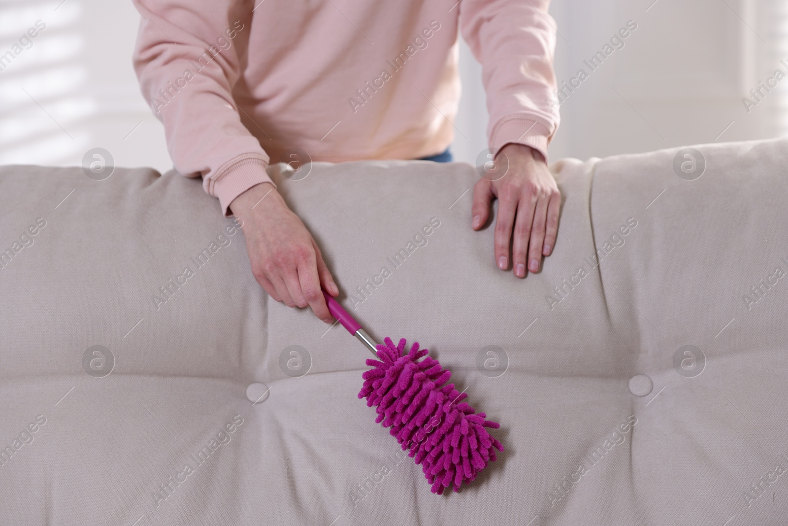 Photo of Woman cleaning sofa with duster at home, closeup