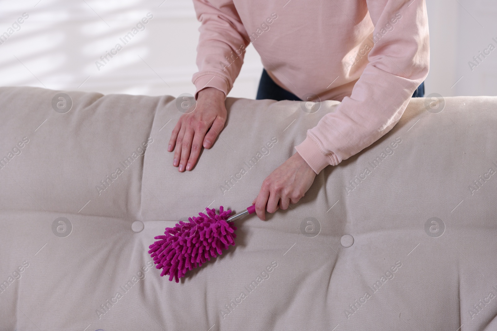 Photo of Woman cleaning sofa with duster at home, closeup