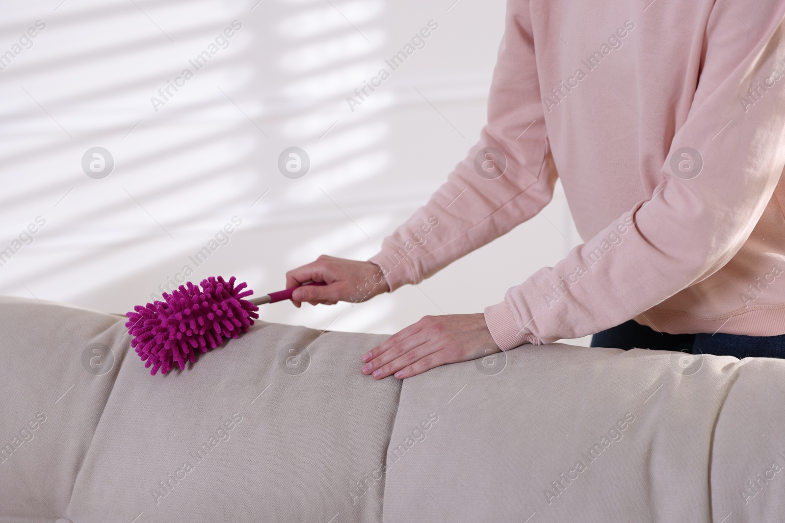 Photo of Woman cleaning sofa with duster at home, closeup