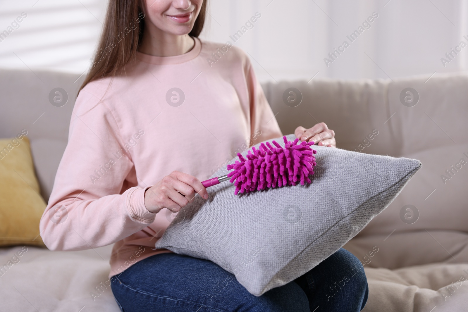 Photo of Woman cleaning sofa cushion with duster at home, closeup