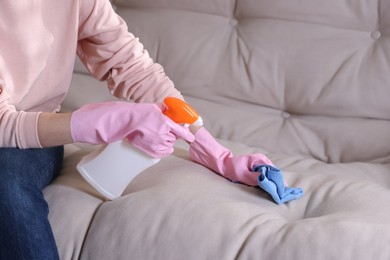 Photo of Woman in gloves cleaning sofa with rag at home, closeup