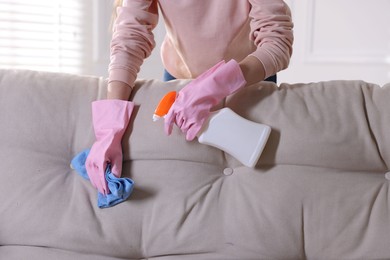 Photo of Woman in gloves cleaning sofa with rag at home, closeup