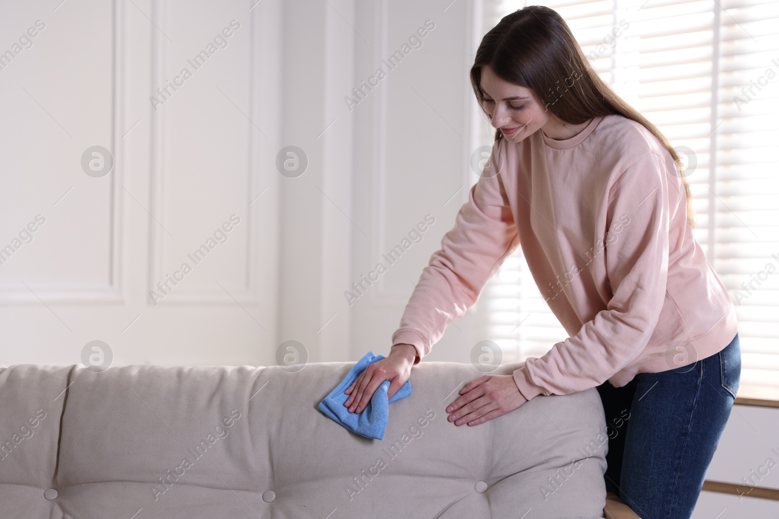 Photo of Happy woman cleaning sofa with rag at home. Space for text