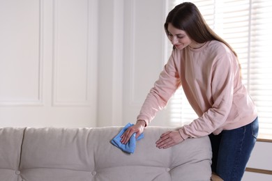 Happy woman cleaning sofa with rag at home. Space for text