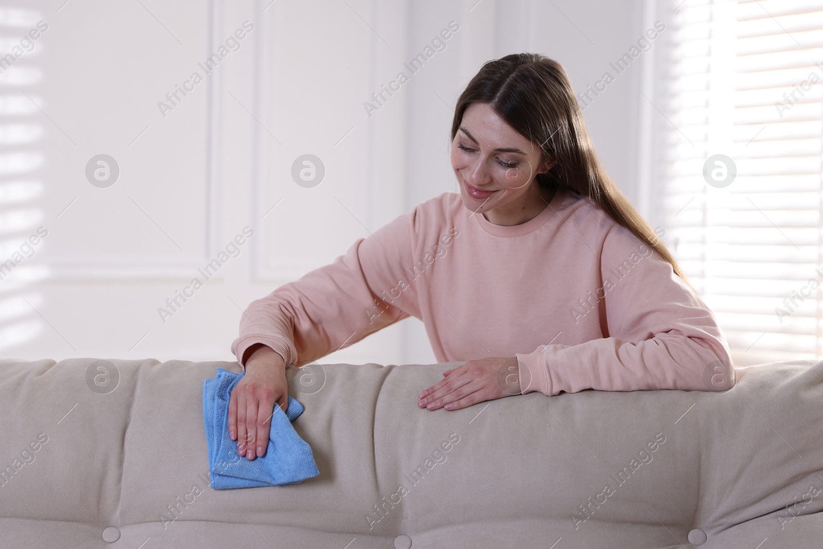 Photo of Happy woman cleaning sofa with rag at home