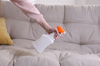 Photo of Woman spraying cleaner onto sofa at home, closeup