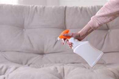 Photo of Woman spraying cleaner onto sofa at home, closeup. Space for text