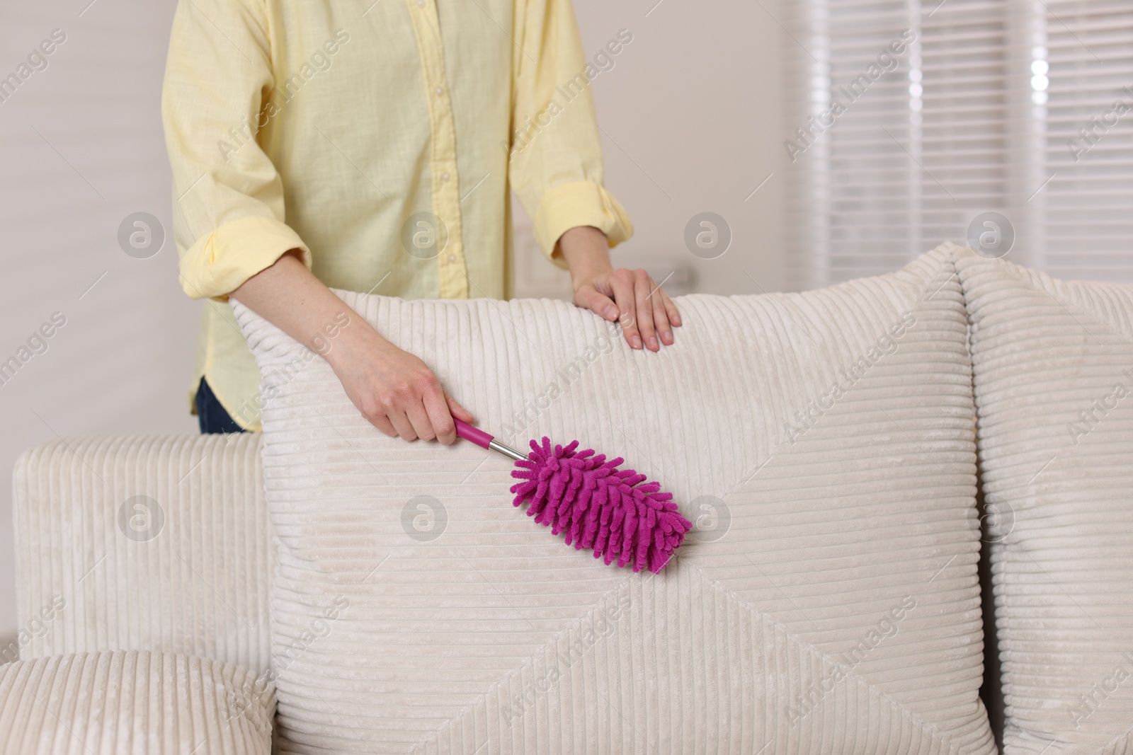 Photo of Woman cleaning sofa with duster at home, closeup