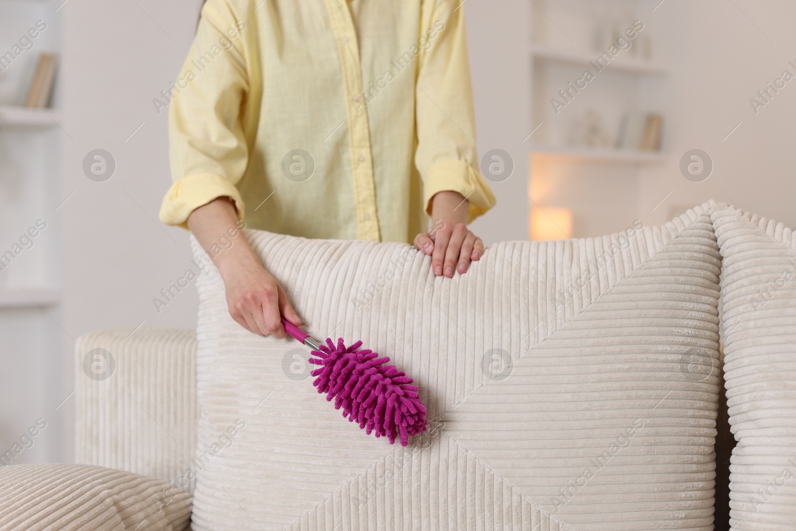 Photo of Woman cleaning sofa with duster at home, closeup