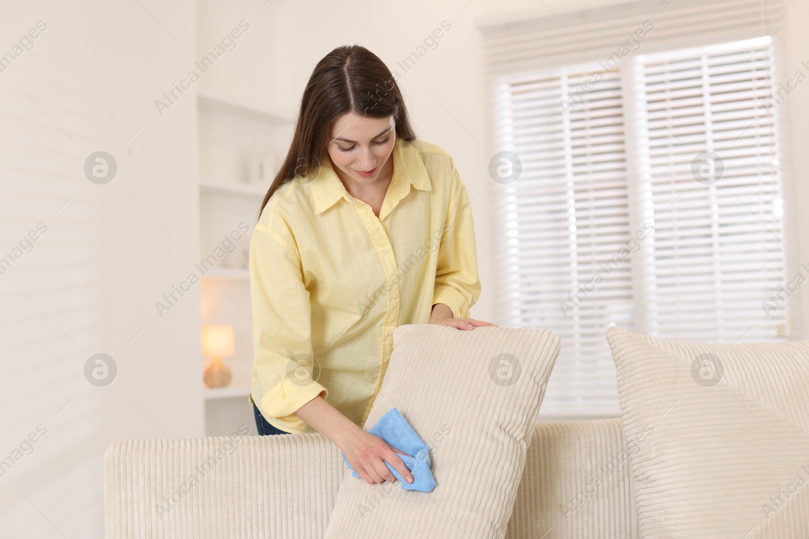 Photo of Happy woman cleaning sofa cushion with rag at home