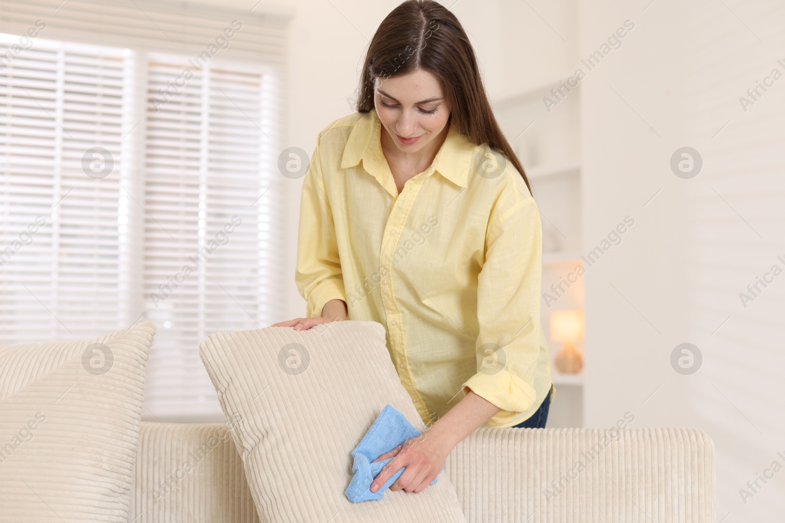 Photo of Happy woman cleaning sofa cushion with rag at home