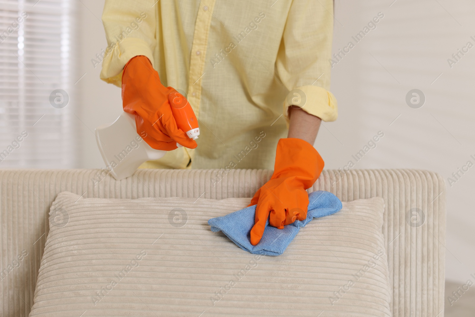 Photo of Woman in gloves cleaning sofa with rag at home, closeup