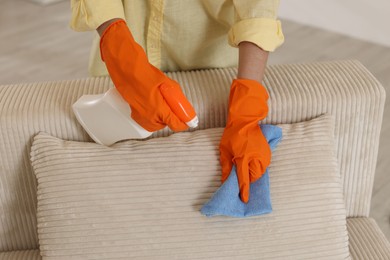 Photo of Woman in gloves cleaning sofa with rag at home, closeup