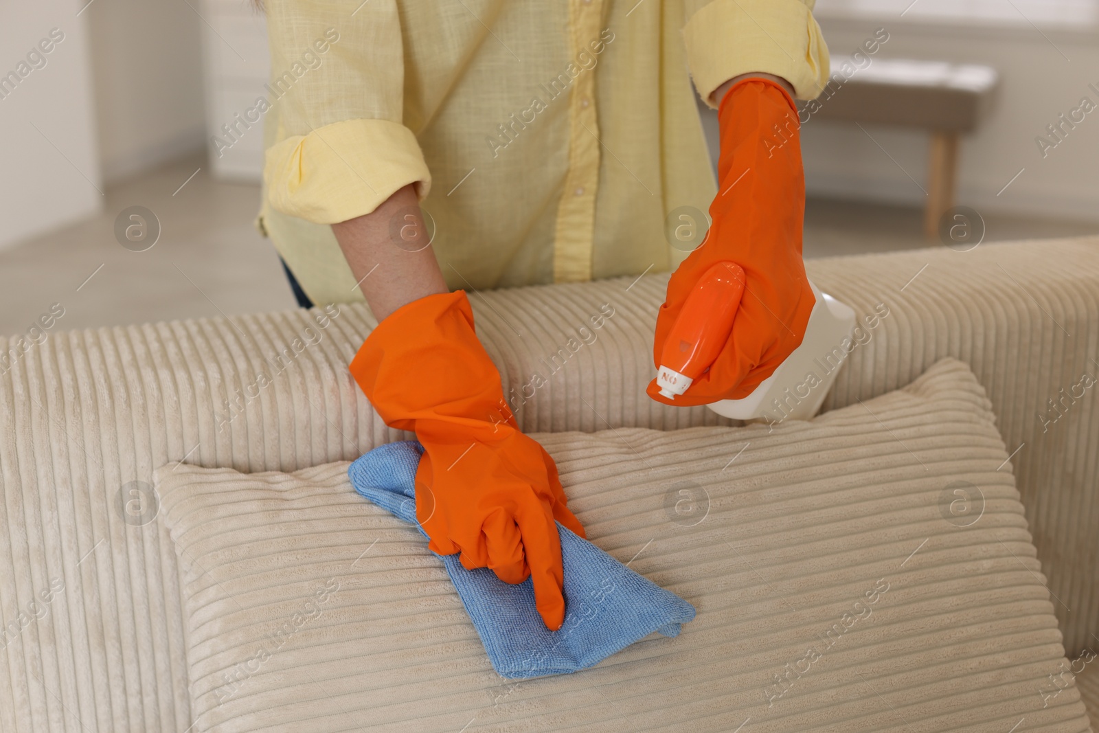 Photo of Woman in gloves cleaning sofa with rag at home, closeup