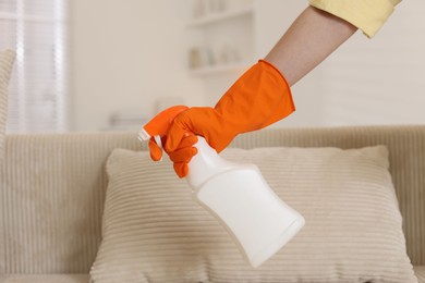 Photo of Woman in glove spraying cleaner onto sofa at home, closeup