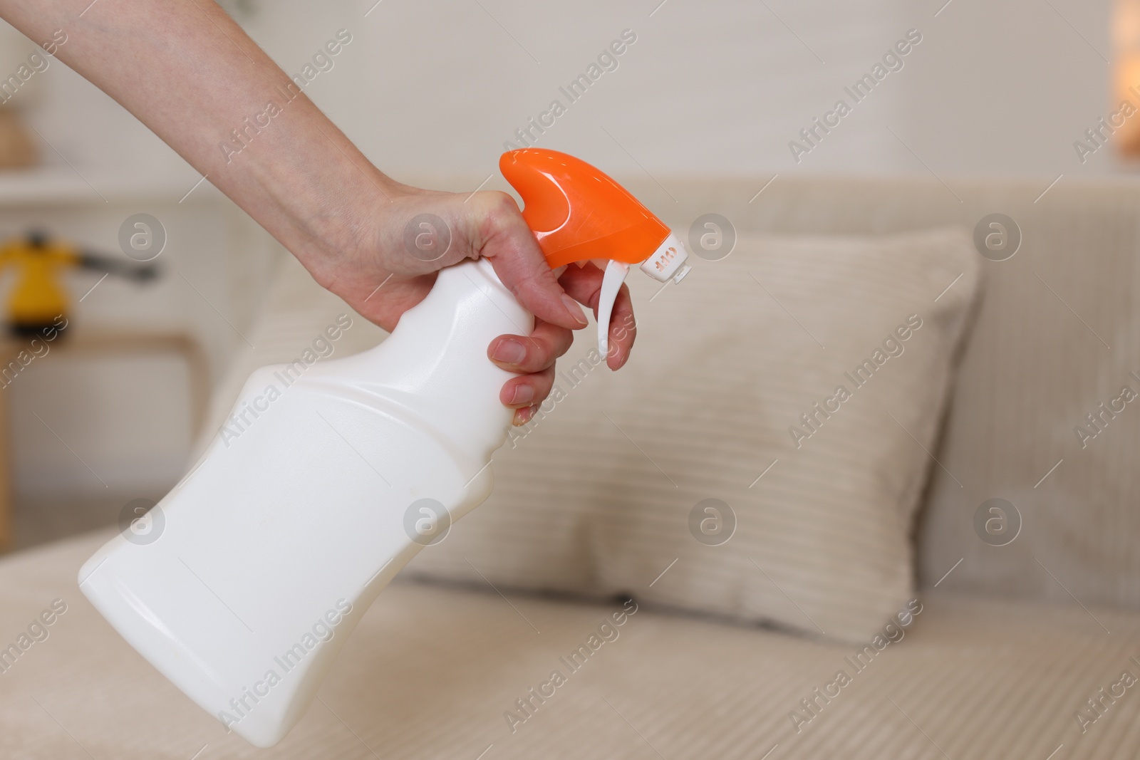 Photo of Woman spraying cleaner onto sofa at home, closeup. Space for text