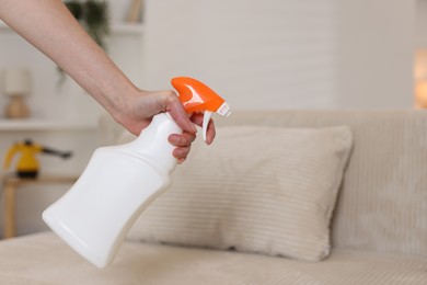 Photo of Woman spraying cleaner onto sofa at home, closeup. Space for text