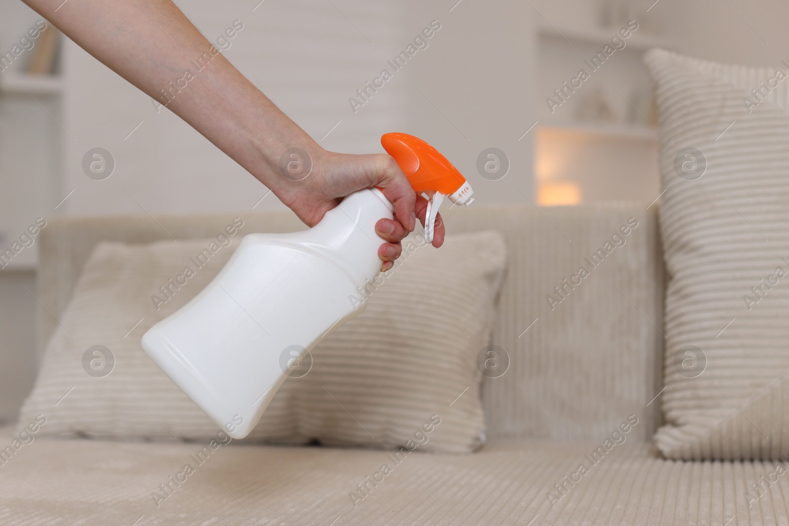 Photo of Woman spraying cleaner onto sofa at home, closeup. Space for text