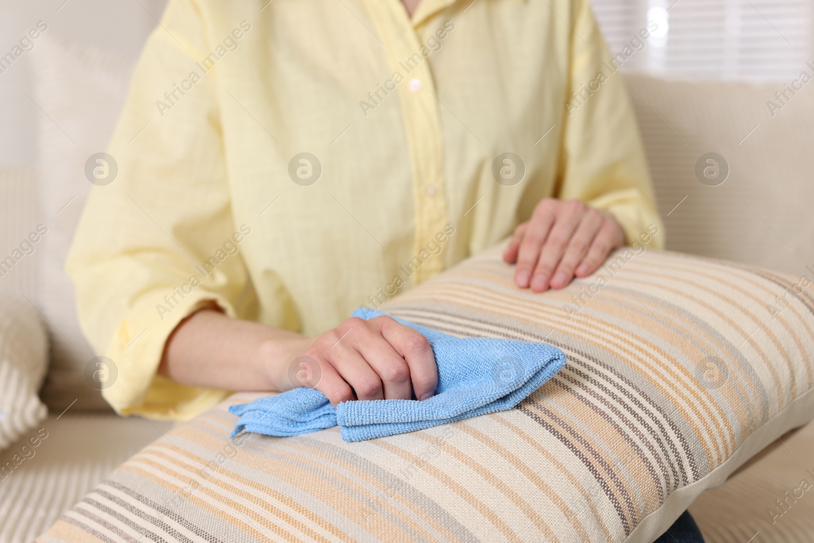 Photo of Woman cleaning sofa cushion with rag at home, closeup