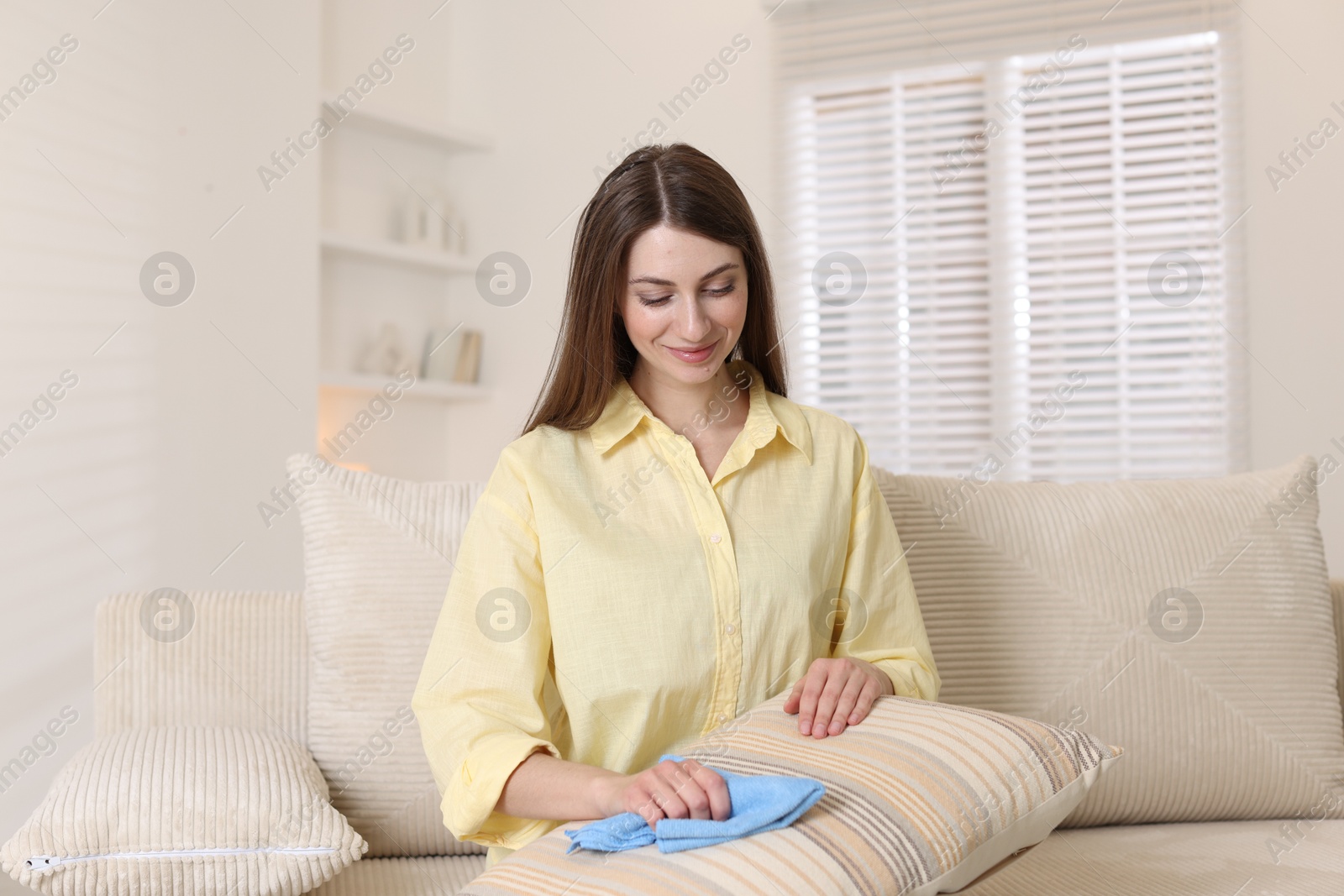 Photo of Happy woman cleaning sofa cushion with rag at home