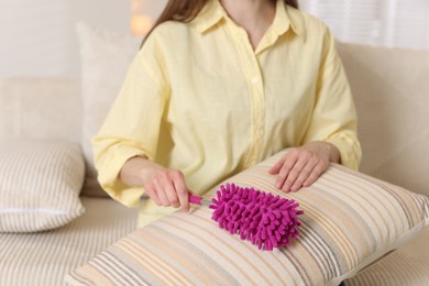 Photo of Woman cleaning sofa cushion with duster at home, closeup