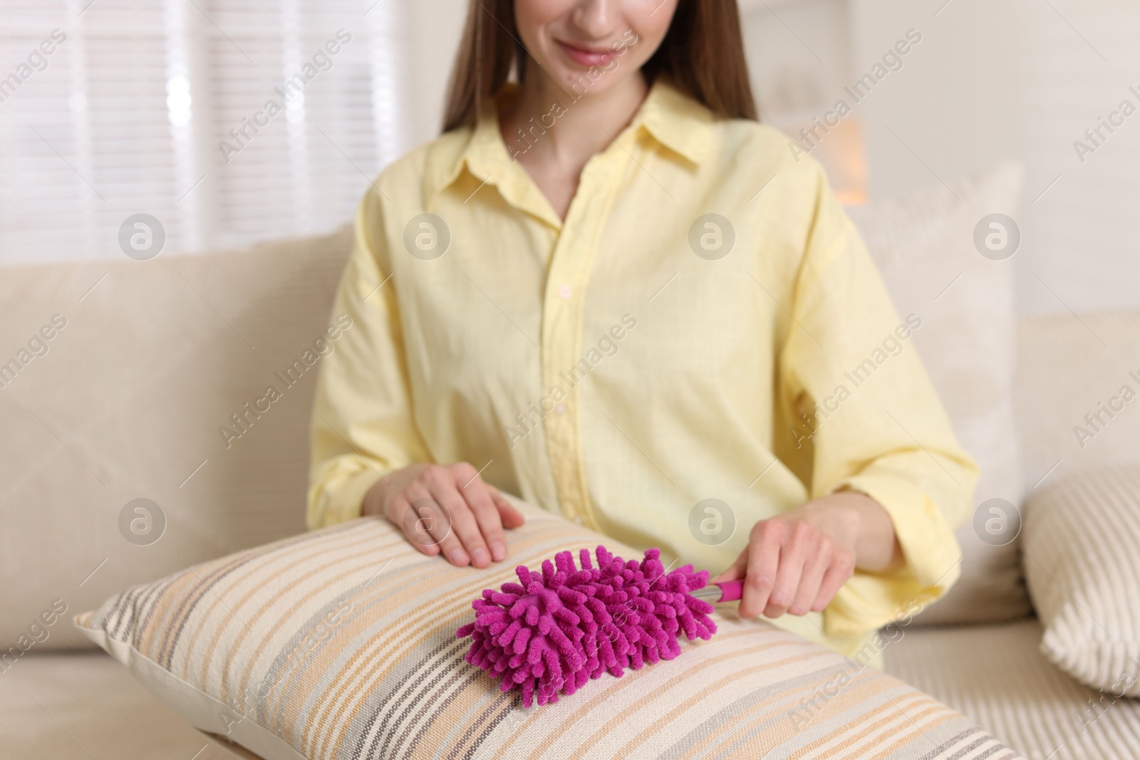 Photo of Woman cleaning sofa cushion with duster at home, closeup