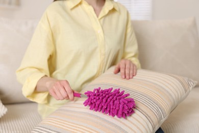 Photo of Woman cleaning sofa cushion with duster at home, closeup