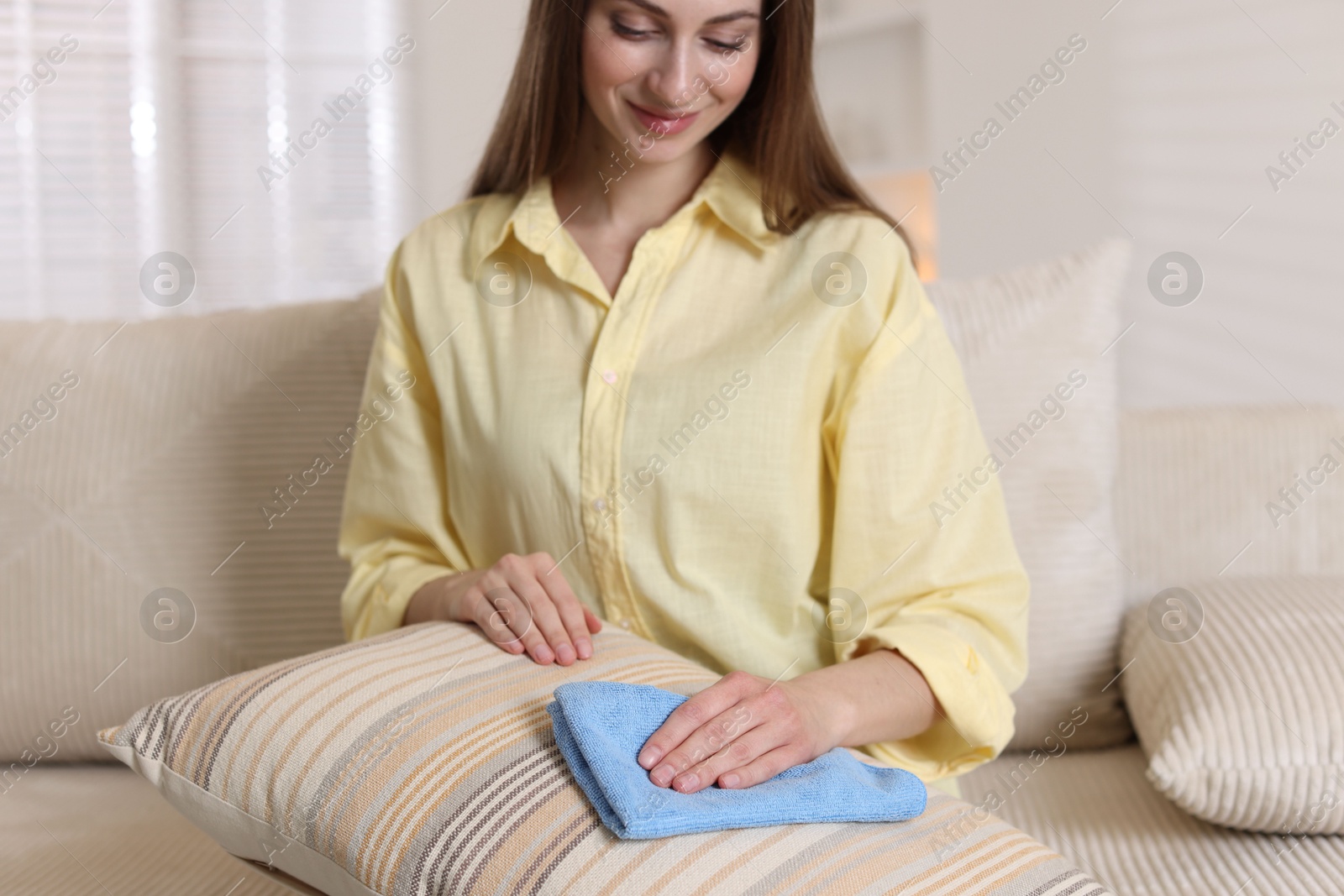 Photo of Happy woman cleaning sofa cushion with rag at home