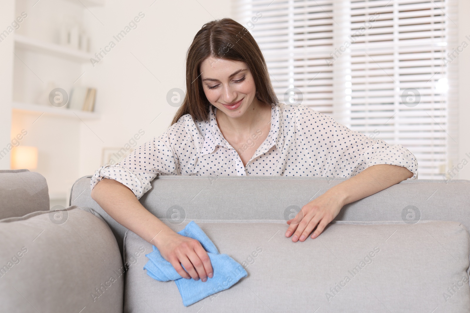 Photo of Happy woman cleaning sofa cushion with rag at home