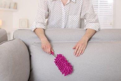 Photo of Woman cleaning sofa with duster at home, closeup