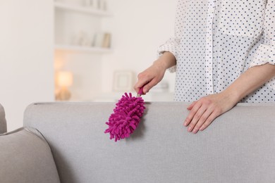 Photo of Woman cleaning sofa with duster at home, closeup