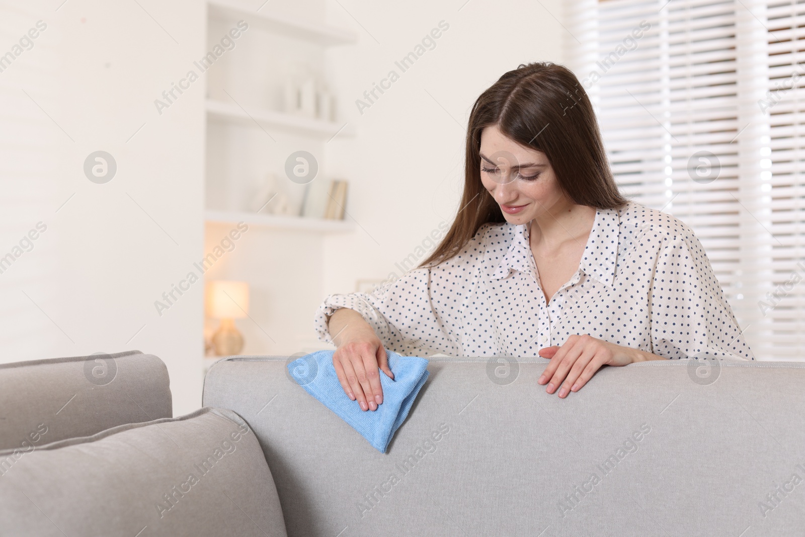 Photo of Happy woman cleaning sofa with rag at home