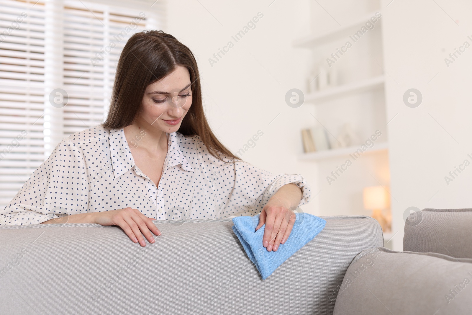 Photo of Happy woman cleaning sofa with rag at home